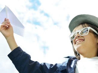 Child holding a paper airplane and dreaming about traveling