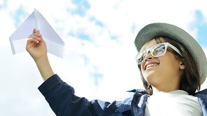 Child holding a paper airplane and dreaming about traveling