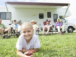 Girl eating an apple with family sitting outside rv