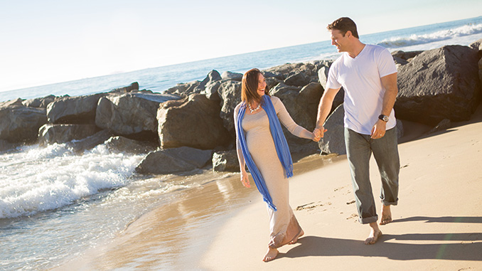 man and pregnant woman walking on beach