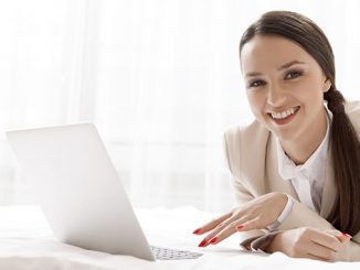 smiling woman with laptop in bed