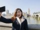 Happy young woman taking self portrait through cell phone against big ben at london, england