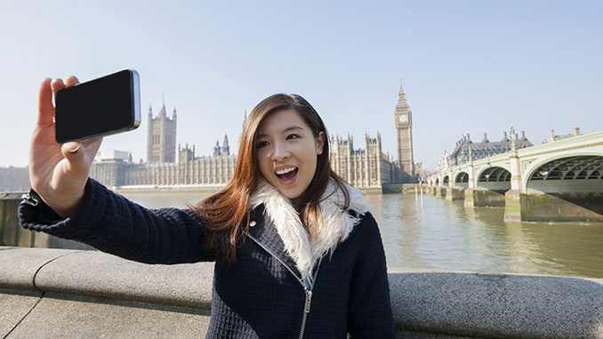 Happy young woman taking self portrait through cell phone against big ben at london, england